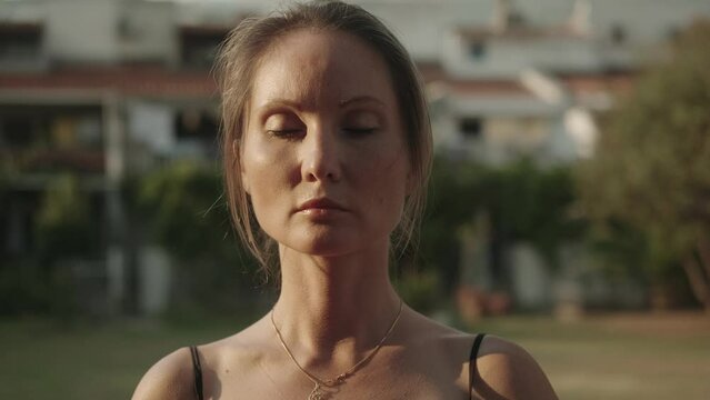 European female qigong master practicing asian breathing exercises with closed eyes outdoors. Close-up. Chinese spiritual and meditation practices. Concentrated attention. Zen. Tai chi. 