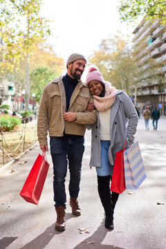 Multiethnic couple in love walking on the street in the city after buying christmas presents, having a good time together outside in winter season. Vertical image.