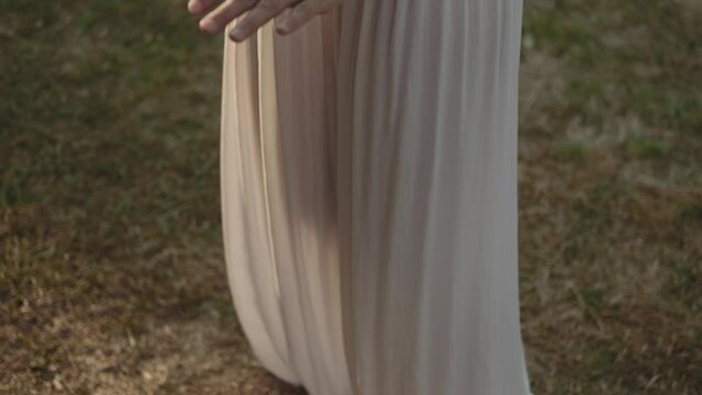 Barefoot woman in white transparent wide trousers practices qigong on the grass. From top to bottom. Knee stretch. Balance of matter, energy and spirit. Asian meditation practice. Taiji. 