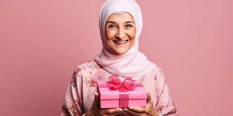 A nice mature arabian woman happily surprised with a gift in her hands with a pink background