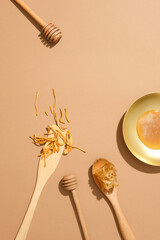 Beige background featured a dish of honey, beeswax, cordyceps and two honey dripping. Flat lay....