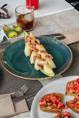 an image of white melon served with jamon serrano alongside tomatoes in a mediterranean restaurant 