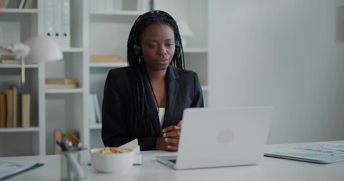 African woman has a video call while sitting at workplace, looking at laptop.