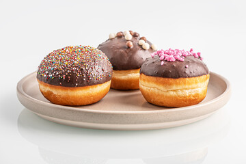 assorted chocolate glazed donuts on ceramic plate on white glass surface close up