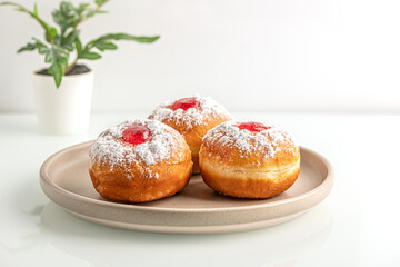 sweet freshly baked donuts with strawberry filling on ceramic plate on white glass surface close up