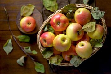 Apples in a basket on a wooden table. Fresh red apples with green leaves on a black background. Fruits. View from above.
