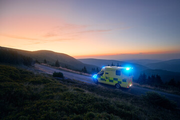 Ambulance car of emergency medical service mountain road against sunrise. Moody sky with copy...