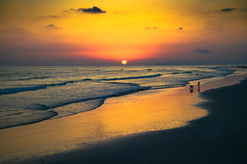 Sunset above Arabian Sea and a beach in Salalah, Oman, against a clear summer sky with silhouettes of people