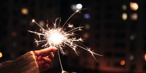 Hand holding burning Sparkler blast on a black  background at night city windows, holiday...