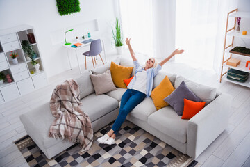 Photo portrait of attractive pensioner woman raise hands have fun sit sofa living room modern interior decoration