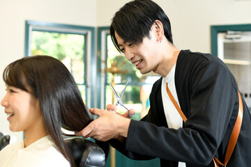 女性客の髪を切るアジア人の男性美容師