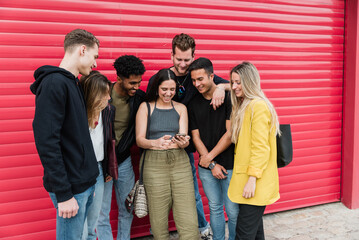 Cheerful diverse friends standing together and looking at smartphone with young woman