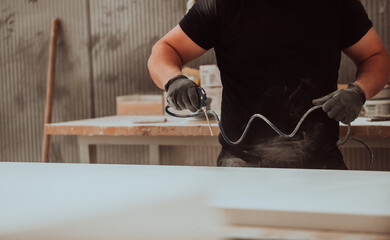 A dedicated worker in the woodworking industry employs compressed air to meticulously clean wooden products in their final stage, exemplifying precision and attention to detail in the craftsmanship