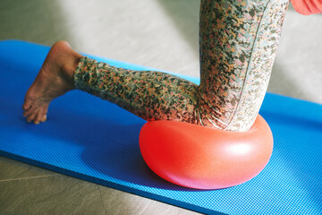 Mature woman practicing balance pose during pilates training, using soft ball for knee