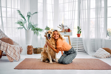 Cheerful woman kneeling on floor to provide strong hugs to her lovely purebred dog. Happy golden...