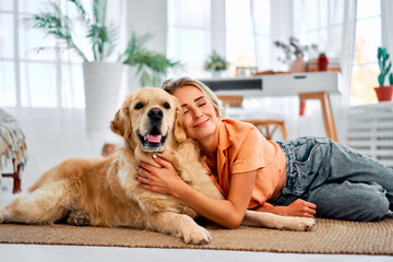 Love for your pet. A golden retriever lies on the floor in the gentle arms of his loving owner. A happy woman with closed eyes shows tenderness and care for a dog.