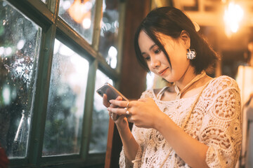 Young adult asian woman using mobile phone for online app at indoor cottage cafe with warm light