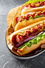 Homemade hot dogs with sausage, green salad, cucumber and red onion on the grey background close up vertical photo