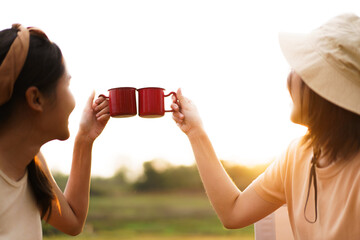 Friends camping in the lake forest and enjoy drinking a cup of tea or coffee. 