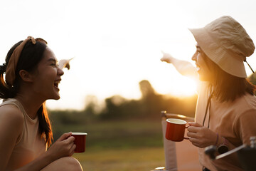 Friends camping in the lake forest and enjoy drinking a cup of tea or coffee. 