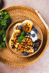 Homemade waffles with blueberries, chocolate sauce and cream cheese in a plate and a beige background top view vertical photo