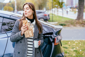 Elegant woman enjoys tasty nutritional snack bites burger with close eyes waiting in city station...