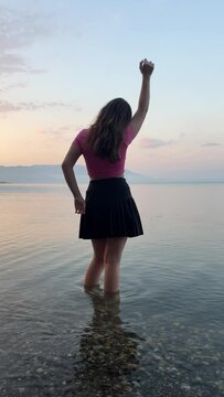 silhouette of young slender girl in water clear water against horizon girl dancing having fun. teenager young woman with hair big pebbles in water blue sky early morning travel photo shoot