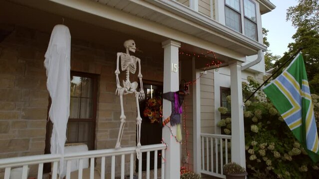Boom down the side of a two story house in the suburbs to reveal halloween decorations on the front porch and a flag.