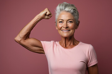 Beautiful cheerful middle aged senior woman with healthy lifestyle, smiling and flexing arm muscles on pink background, health and wellness for aging society concept. - obrazy, fototapety, plakaty