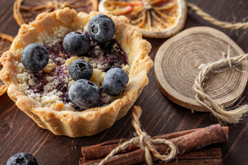 French dessert. Little tart with fresh berries. Tartlets with blueberries, cinnamon, dried oranges on dark background.