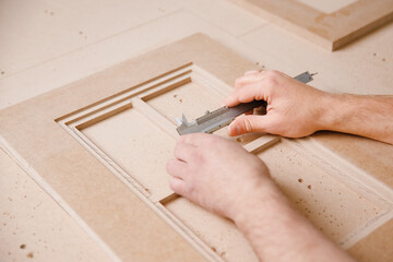 Production of kitchen furniture, worker controlling dimensions on wooden facade from cutting CNC milling machine