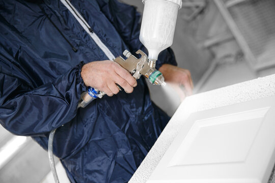 Professional worker staining wood furniture with spray gun