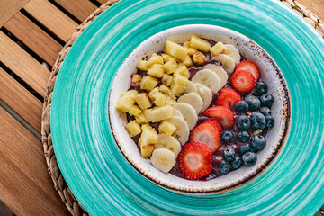 a close up image over a bowl of fresh acai ice cream topped with fresh fruits and berries on a wooden table 