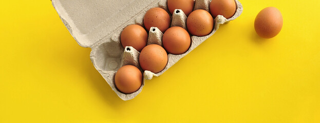 Rustic, organic brown chicken eggs in an open sustainable cardboard tray (box) on a bright, monochrome yellow background. Playful festive image. No people. Copy space