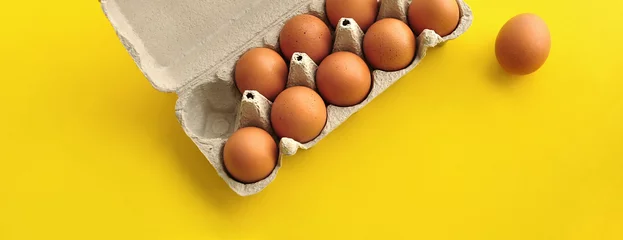 Foto op Plexiglas Rustic, organic brown chicken eggs in an open sustainable cardboard tray (box) on a bright, monochrome yellow background. Playful festive image. No people. Copy space © Gintare Stackunaite