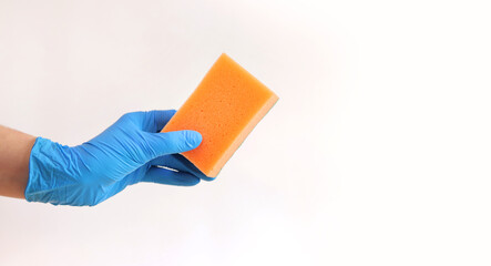 Orange dishwashing sponge in a woman's hand on a gray background. A hand in a latex blue glove holds a sponge for wet cleaning. Professional cleaning. Copy space