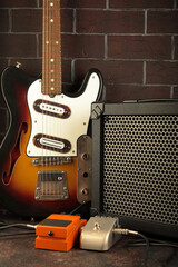 Vintage electric guitar, guitar amplifier and effects pedals for the guitarist on a dark brick background.