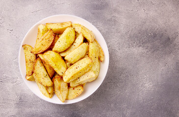 Baked potato wedges with seasonings on a plate on a gray stone.
