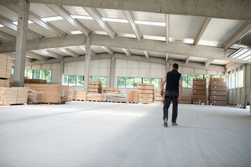 A worker leisurely strolls through a warehouse housing a diverse array of wooden products,...
