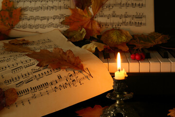 lit candle and autumn leaves, piano, music paper - 689127568