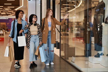Full shot of multiracial group of young girls walking around shopping mall observing shop windows