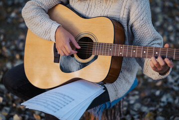 Girl musician practicing playing the guitar outdoor, looking to sheet with chords. Girl playing the...