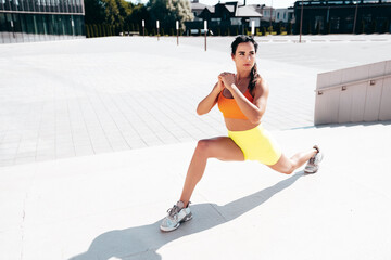 Fitness woman in sports clothing. Sexy young beautiful model athlete doing fitness workout. Female making exercises in the street at sunny day. Stretching out before training. at stairs. Makes lunges