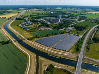 Fototapeta premium Drone Shot of solar panels at a sunny day between fields, river and a street.