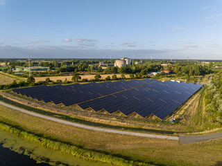 Drone Shot of solar panels at a sunny day between fields, river and a street.