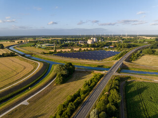 Drone Shot of solar panels at a sunny day between fields, river and a street.