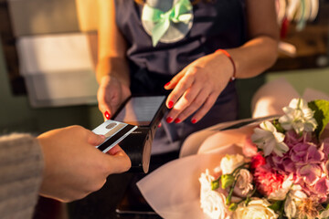 Close up of female hands using credit card for paying using payment terminal in flower shop.