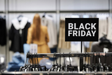 Black friday sign attached to clothing rack at store with customer choosing clothes on background