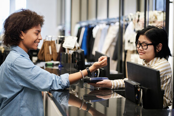 African american woman paying for her purchases with smartwatch, asian cashier receiving payment