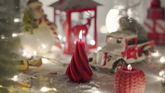 A Christmas candle in the shape of a fir tree burns with a uniform warm flame. A festive atmosphere in a miniature snow-covered town.